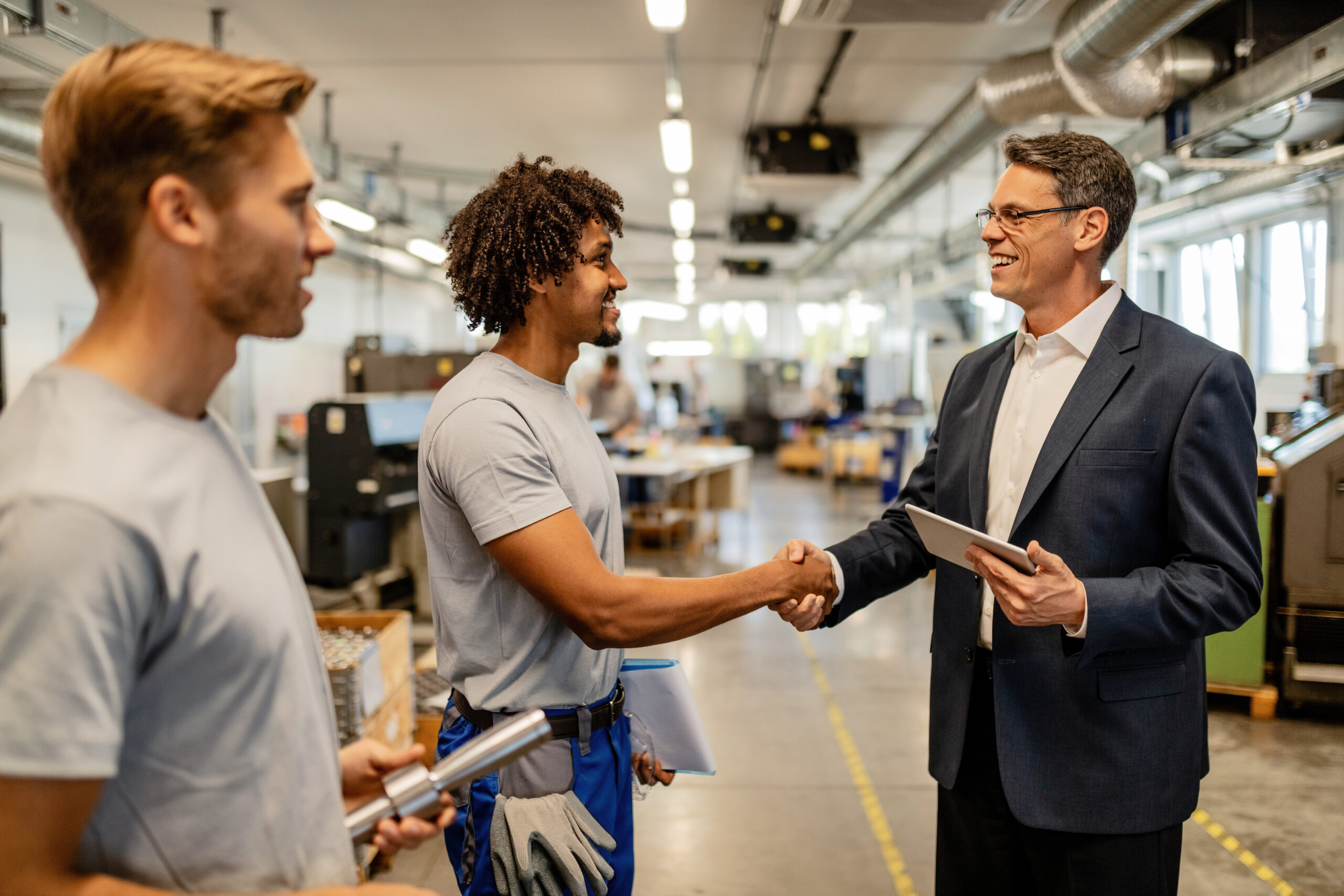 Happy African American worker greeting with quality control inspector in industrial building.
